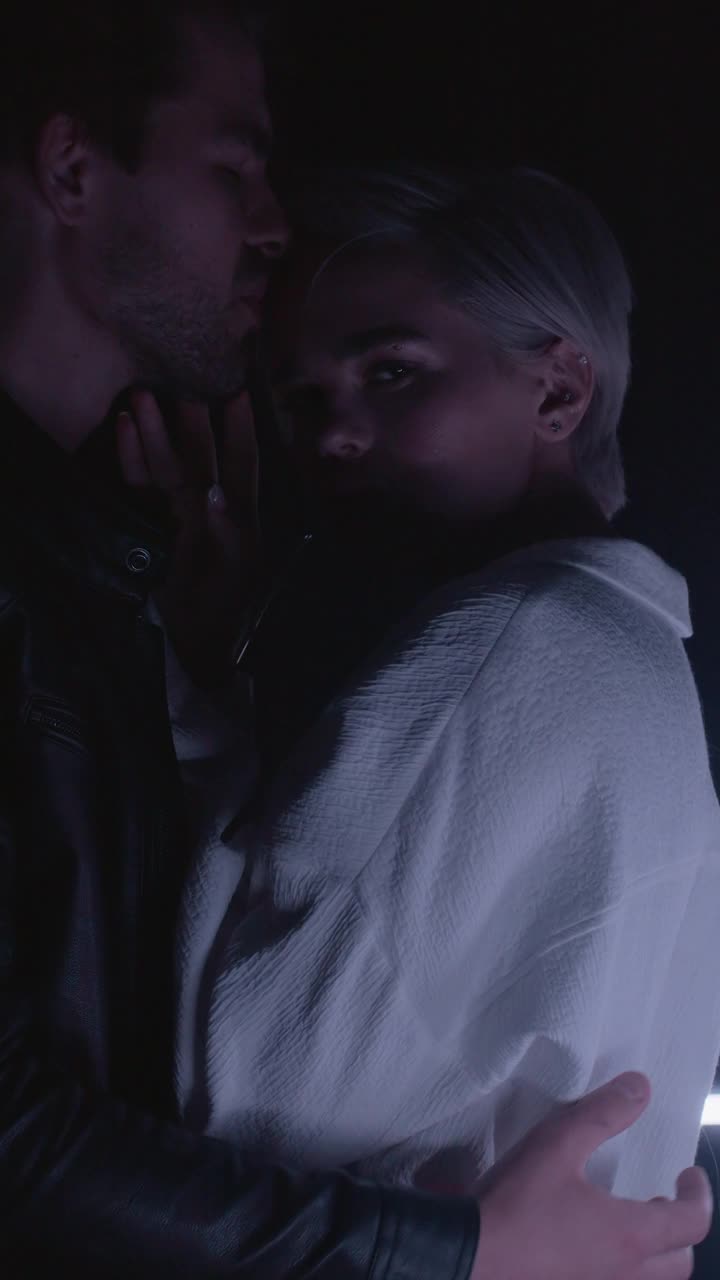 年轻感性夫妇的肖像拥抱，亲吻在现代动态光室内近视频素材