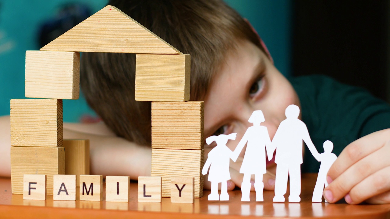 一个6-7岁的白人男孩手里拿着一个家庭的剪纸剪影。碑文出自木字世家，孩子们在木块砌成的房子里玩耍。有选择性的重点视频下载
