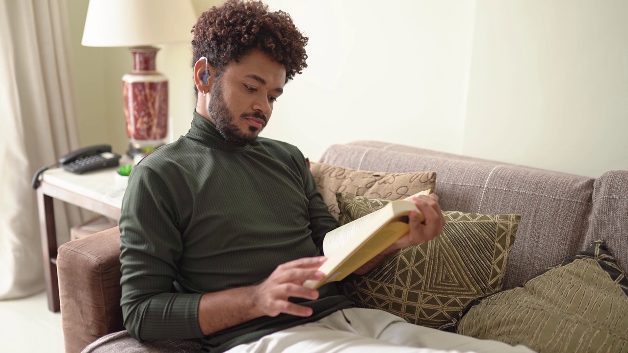 一个年轻人在家里的沙发上看书放松视频素材