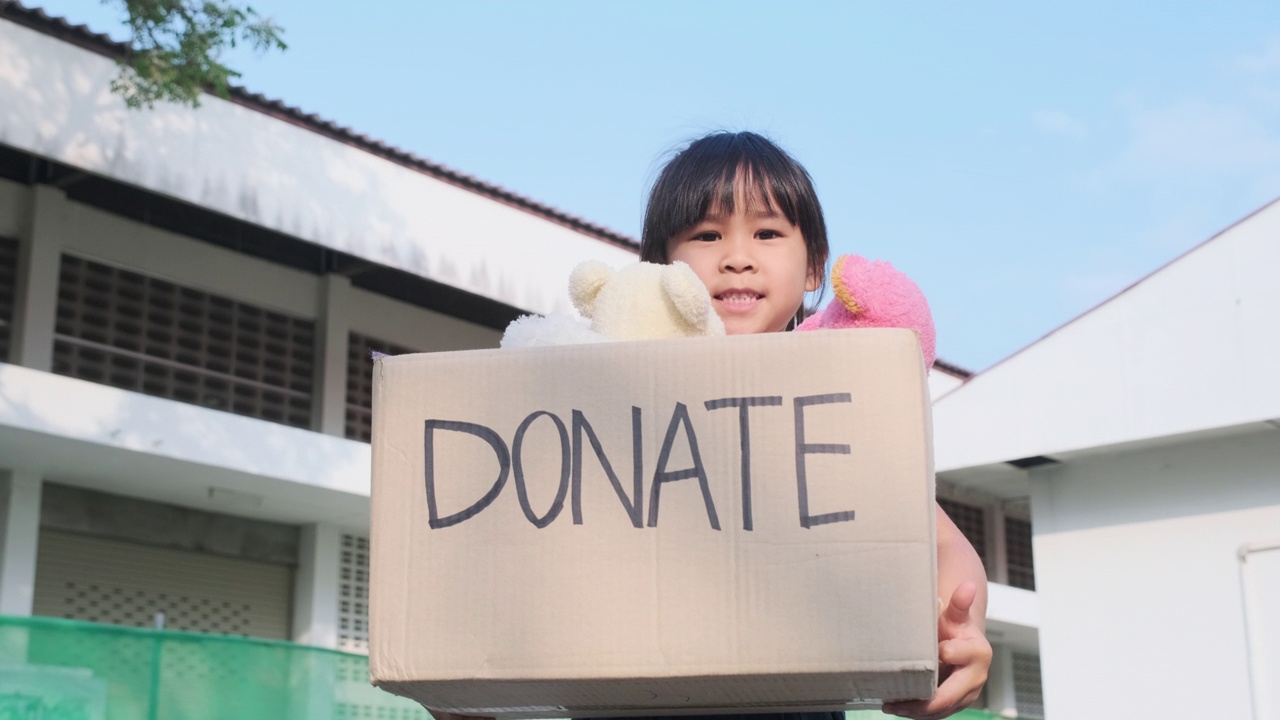 可爱的姐妹女孩拿着捐款箱和旧娃娃在户外。捐赠的概念。视频下载