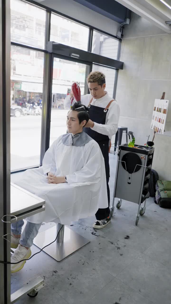 亚洲男性美发师在美容院用吹风机吹干帅气男性客户的短发。视频素材
