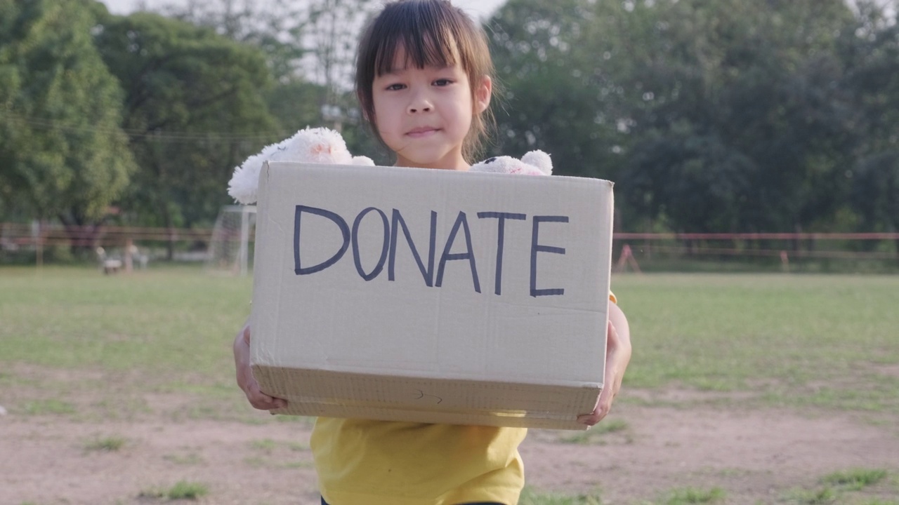 可爱的小女孩拿着捐款箱和旧娃娃在户外。捐赠的概念。视频下载