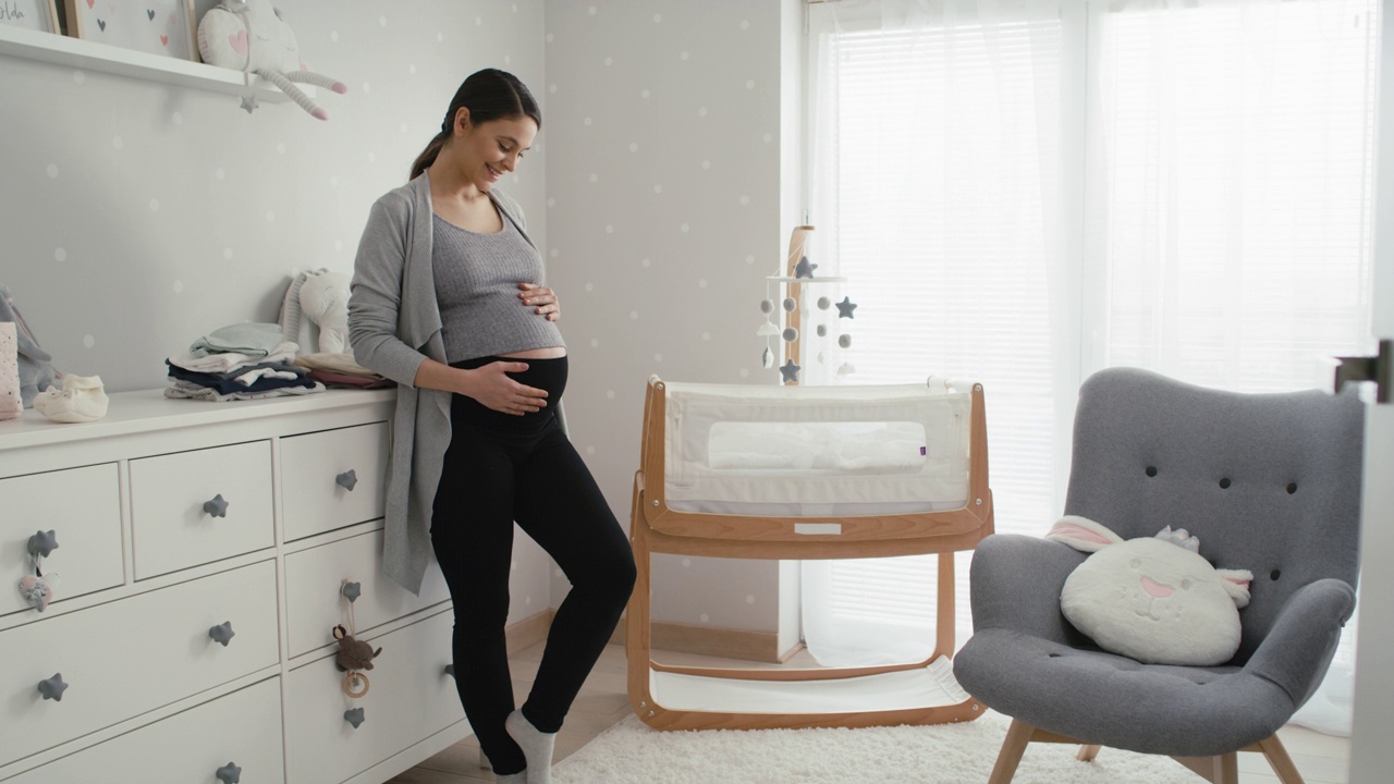 怀孕晚期的白人妇女站在婴儿房的婴儿床旁边。用8K的红色氦相机拍摄。视频下载