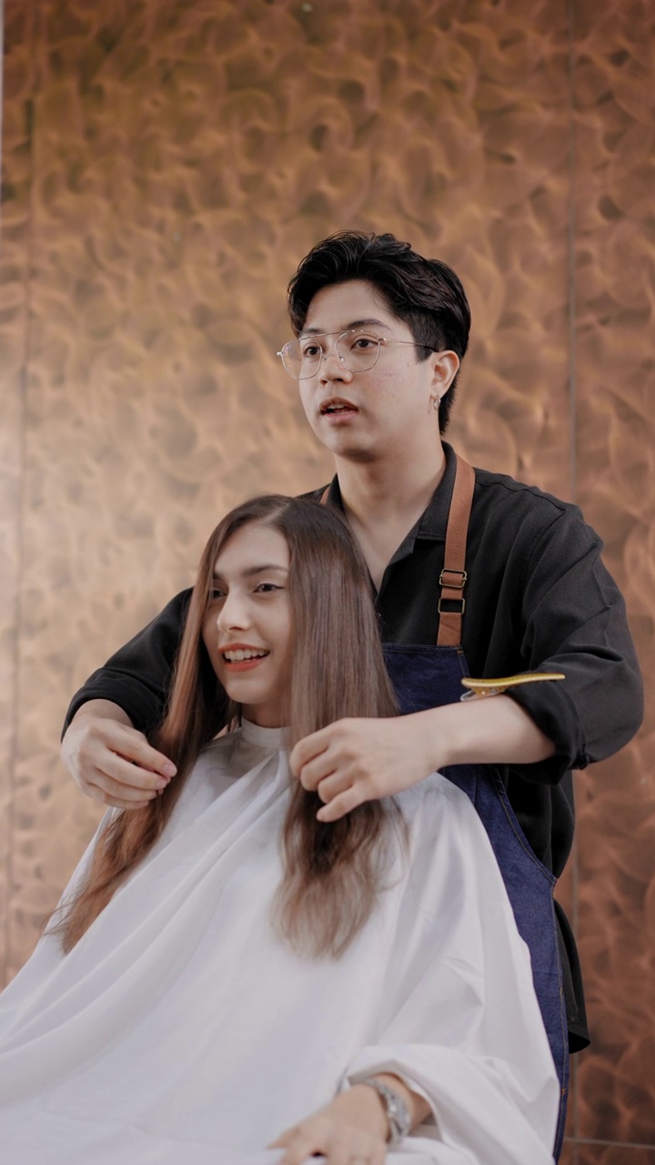 专业的亚洲男性美发师在美发厅理发师设计微笑的美丽的年轻女士的发型，明亮的棕色视频素材