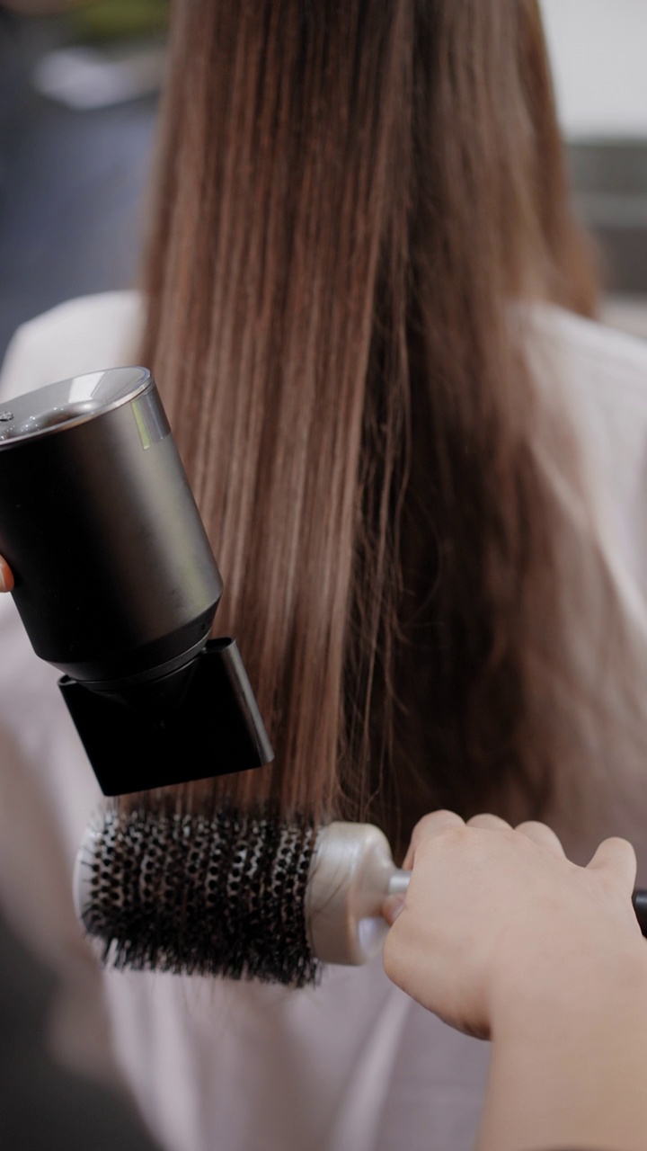 美发师的后视镜是在美发沙龙用电吹风吹干女客户的长发，使头发变直。视频素材