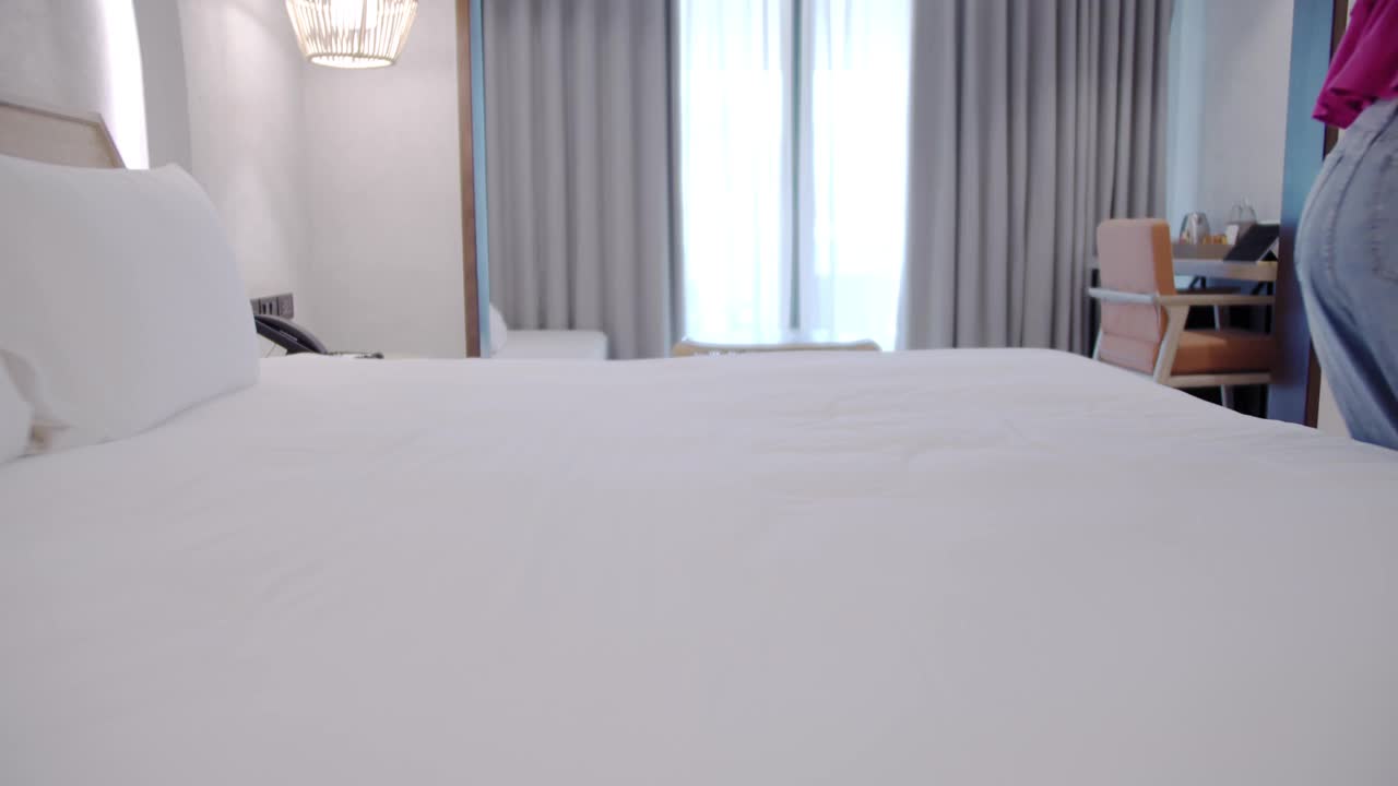 周末假期，亚洲旅游女性在入住酒店后，喜气洋洋地跳上酒店房间的床。视频下载