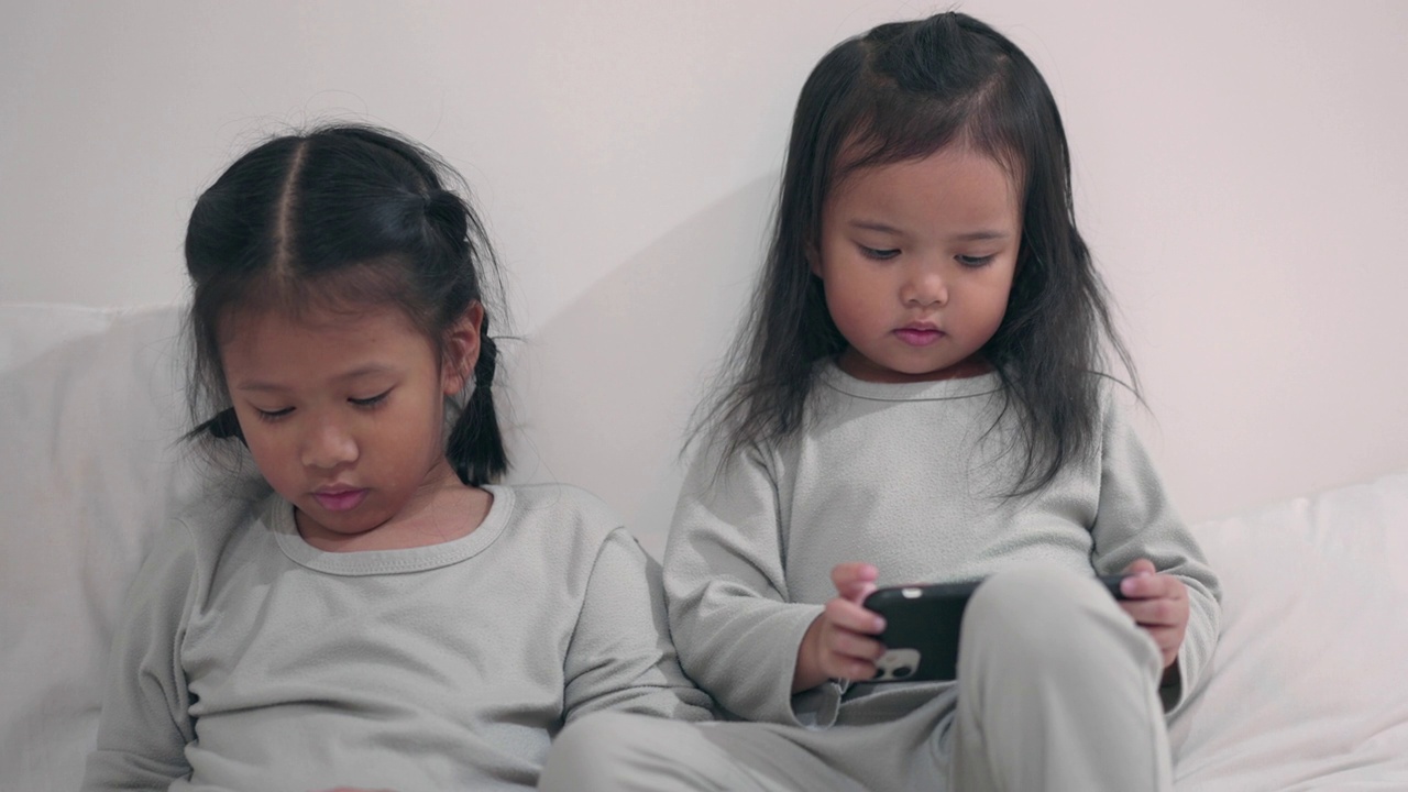 孩子们坐在床上玩手机游戏视频素材