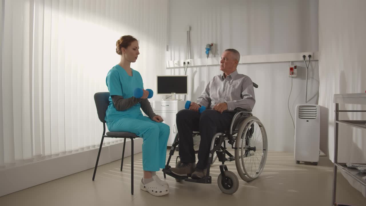 年轻的护士用哑铃帮助坐轮椅的病人进行体育锻炼视频下载