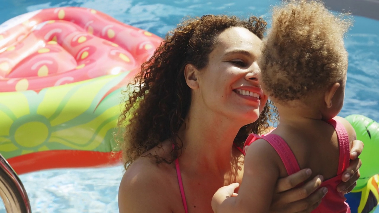 快乐的妈妈和宝贝女儿在阳光明媚的夏日游泳池视频素材