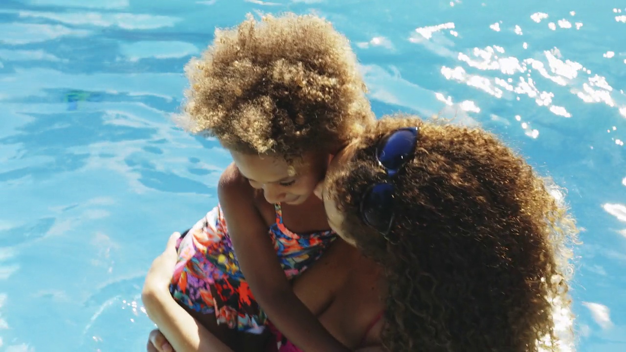 慈祥的母亲和蹒跚学步的女儿在阳光明媚的夏日游泳池视频素材