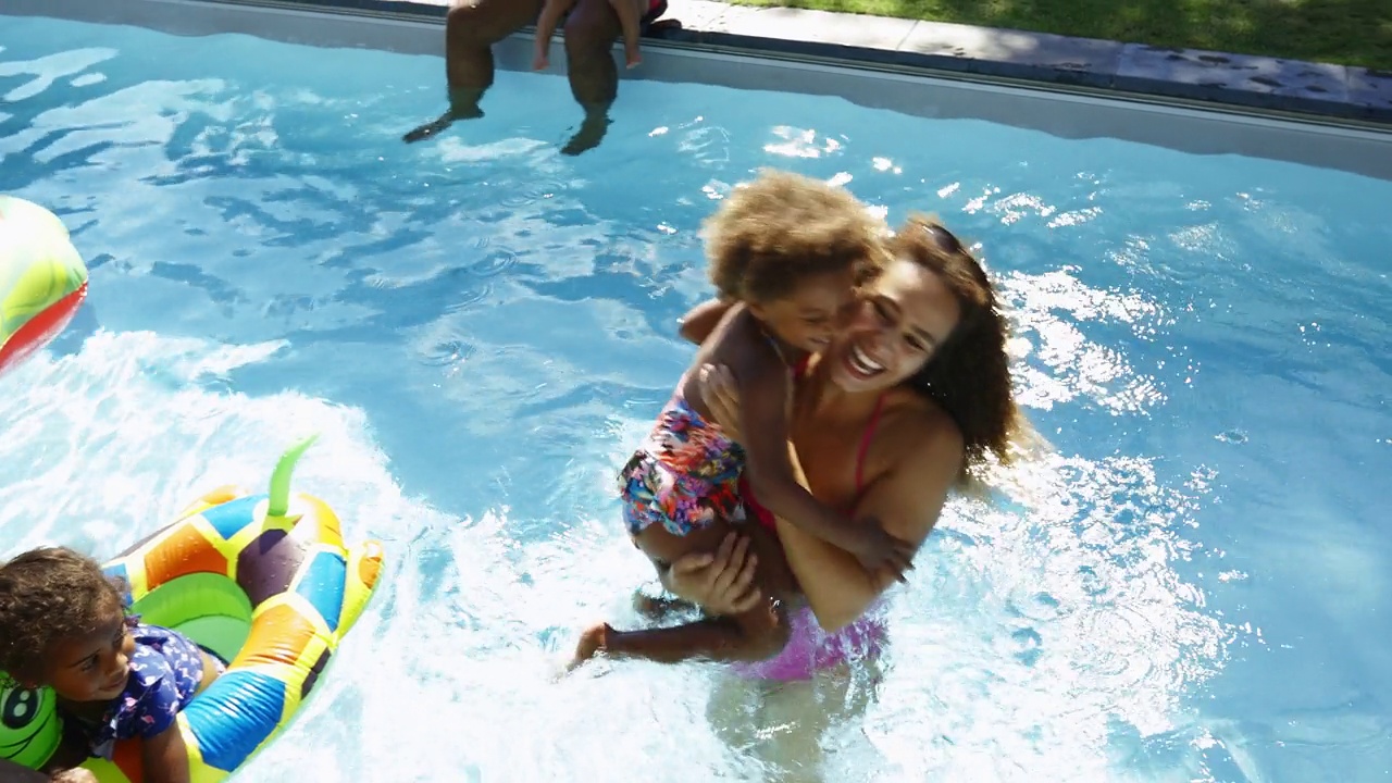 在阳光明媚的夏日游泳池里，女儿跳入妈妈的怀抱视频素材