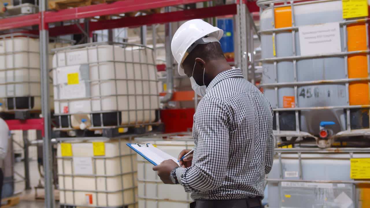 非洲经理戴着安全帽，带着剪贴板在大仓库里做库存视频下载
