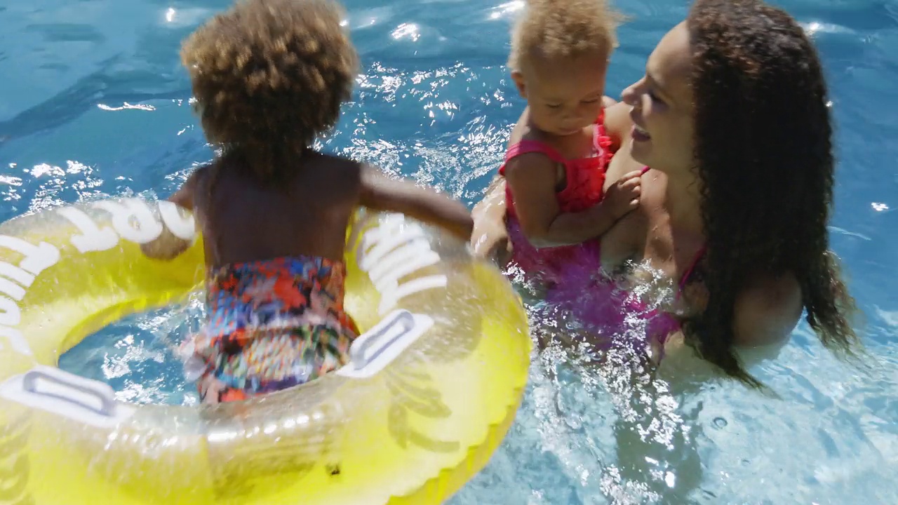 妈妈和女儿在阳光明媚的游泳池里玩着游泳池筏视频素材