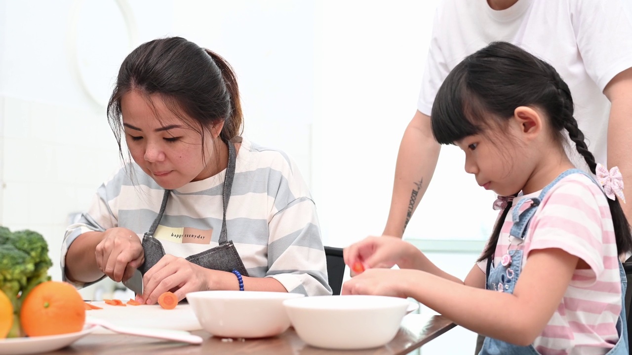 快乐的亚洲母亲和女儿坐在餐桌前一起准备饭菜的肖像视频下载