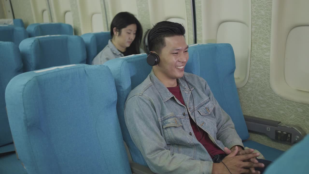 亚洲旅客在飞机上看电影或听音乐在飞行途中戴着耳机视频素材