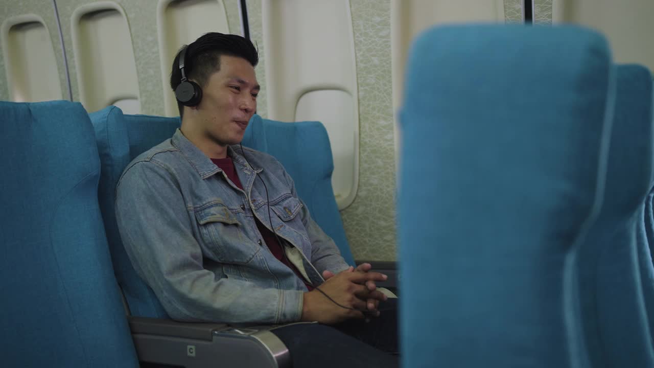 亚洲旅客在飞机上看电影或听音乐在飞行途中戴着耳机视频素材