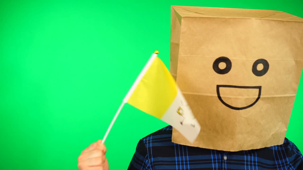 头上戴着纸袋的男子肖像，在绿色的背景下挥舞着面带微笑的梵蒂冈国旗。视频下载