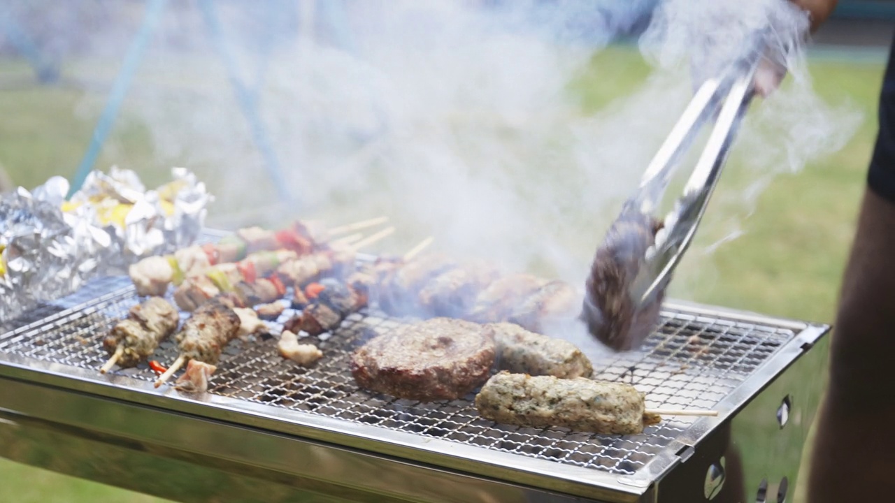 夏日的后院，一名男子在烟雾缭绕的烧烤架上翻肉视频下载