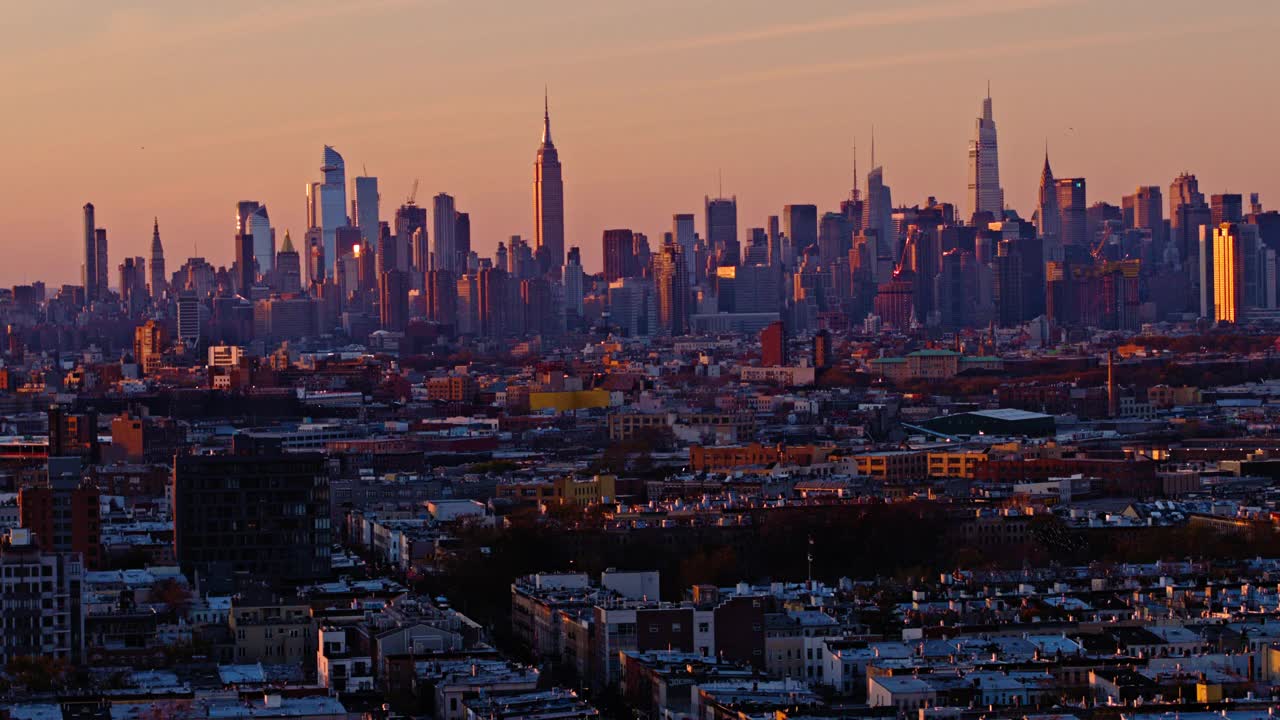 晚上，鸟儿在布鲁克林布什维克住宅区上空飞翔，远处是曼哈顿中城的天际线，背景中有哈德逊广场(Hudson Yards)、帝国大厦(Empire State Building)和其他标志性建筑。平移相机运动。视频下载