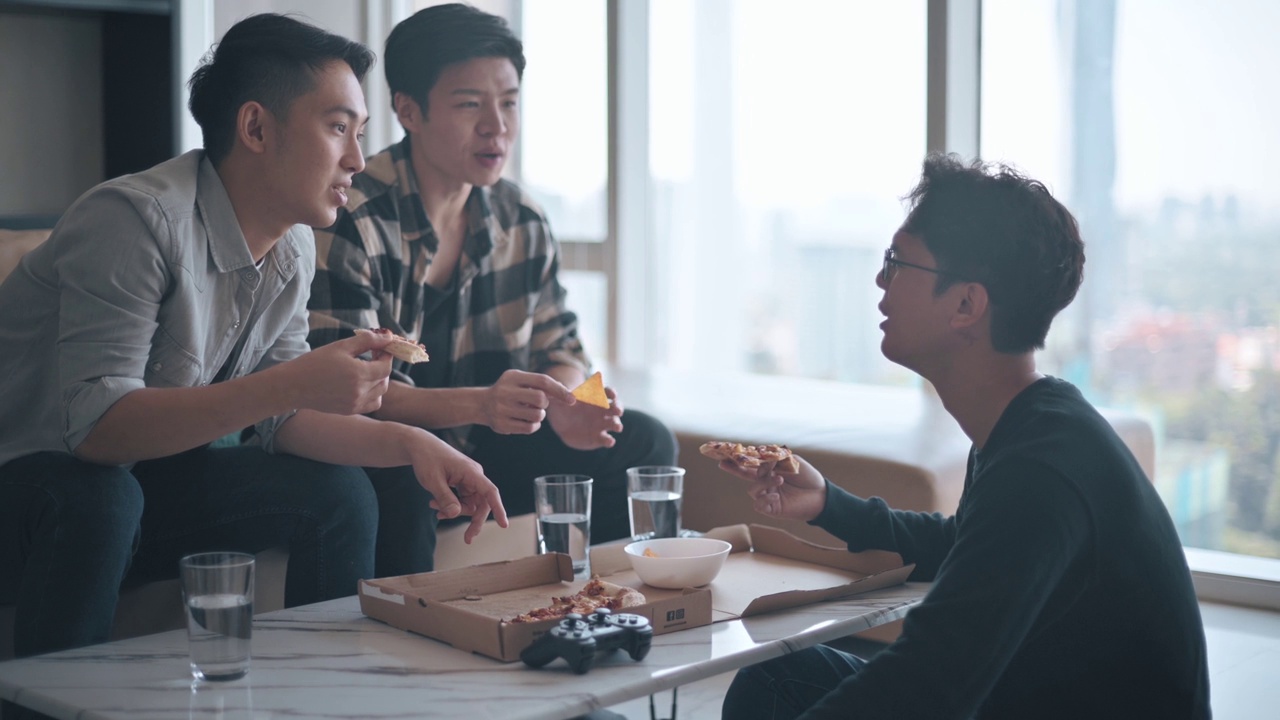 亚洲华人男子与朋友在家中客厅享用快餐披萨视频下载