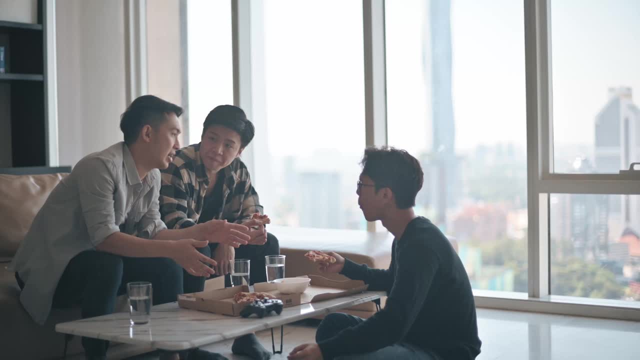 亚洲华人男子与朋友在家中客厅享用快餐披萨视频下载