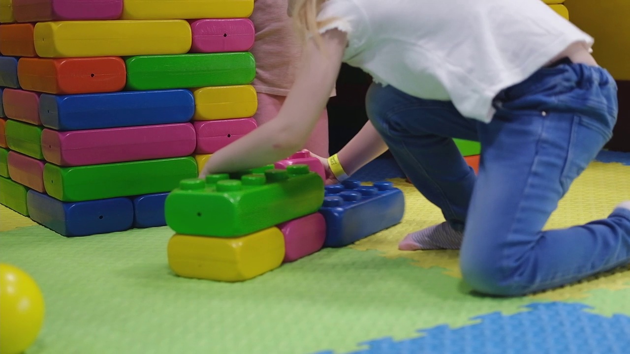一个学龄前的小女孩用彩色塑料玩具砖盖了一个房子。视频下载