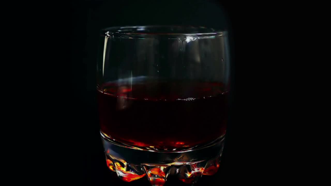 掉落的冰块在一个孤立的黑色背景上落入威士忌酒杯。缓慢的运动。视频下载