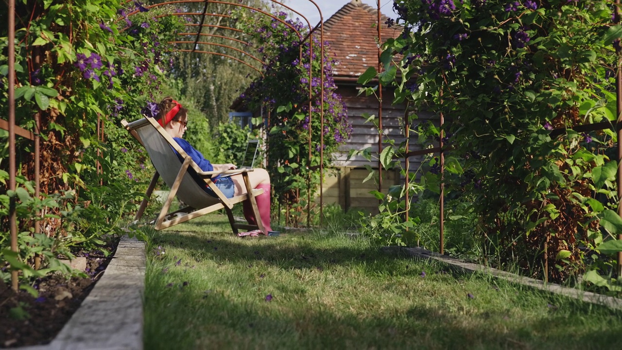 一个女人在阳光明媚的夏日后院花园里使用笔记本电脑视频素材