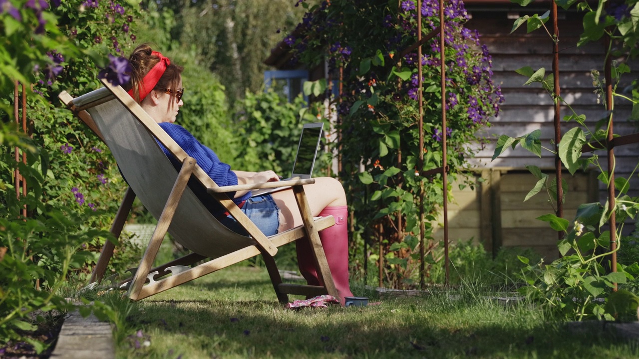 一个女人在阳光明媚的夏日花园里用笔记本电脑工作视频素材