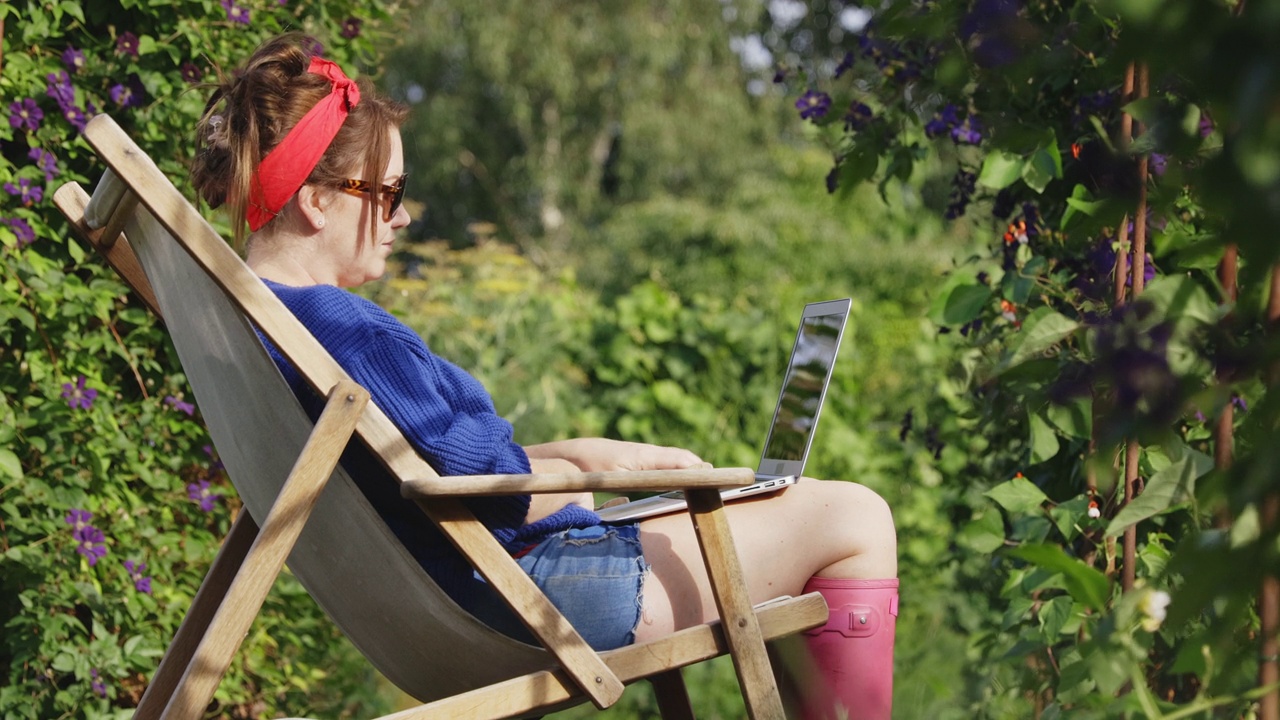 一个女人在阳光明媚的夏日后院花园里使用笔记本电脑视频素材