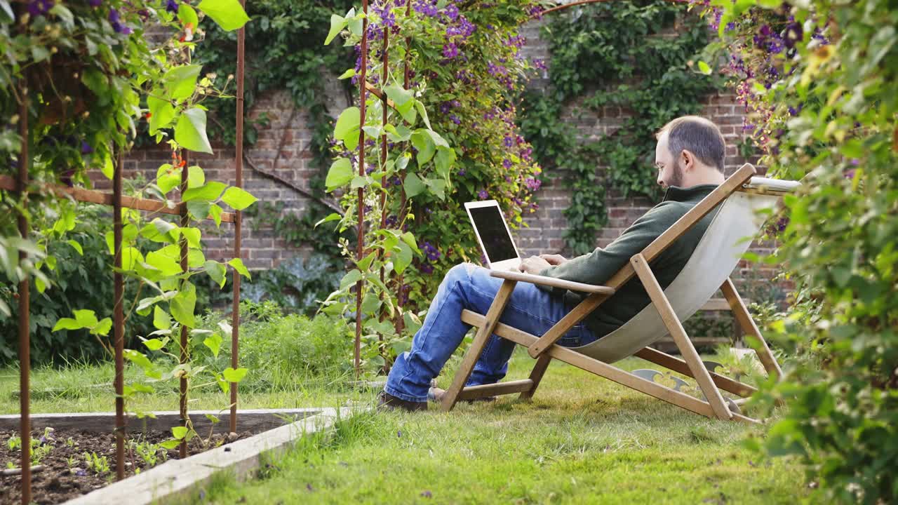 夏日后院花园，男子坐在躺椅上使用笔记本电脑视频素材