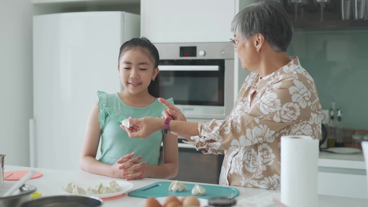 亚洲的中国年轻女孩在周末的闲暇时间在厨房学习她的祖母准备中国饺子视频下载