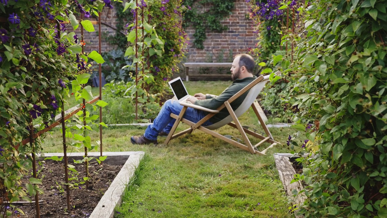 一个人在夏日的后院花园用笔记本电脑工作视频素材