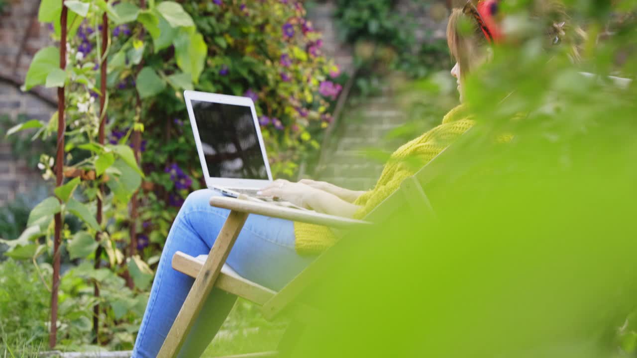 一个女人在夏日的后院花园里使用笔记本电脑视频素材