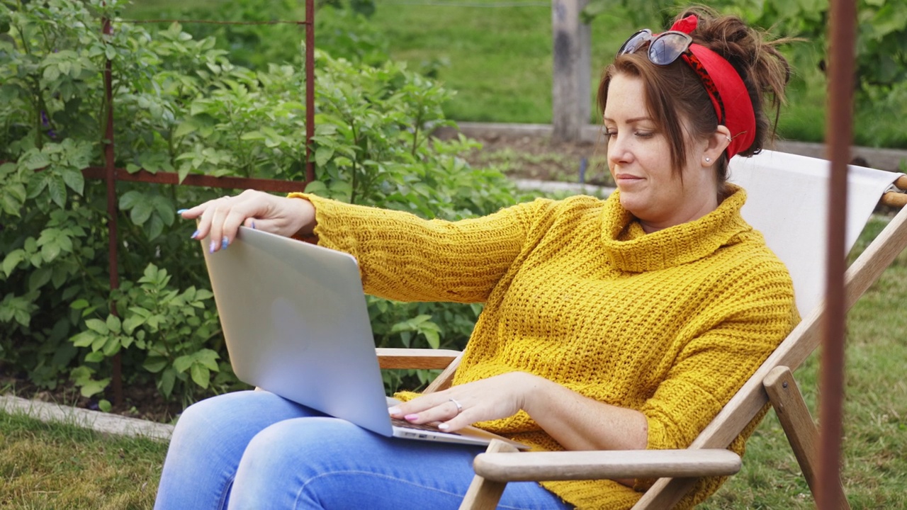 坐在草坪椅上的女人关上笔记本电脑，离开后院花园视频素材