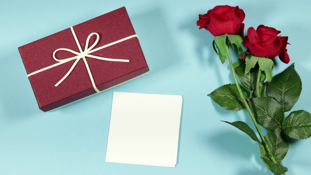礼盒红玫瑰花和白色纸卡在蓝色的背景视频下载