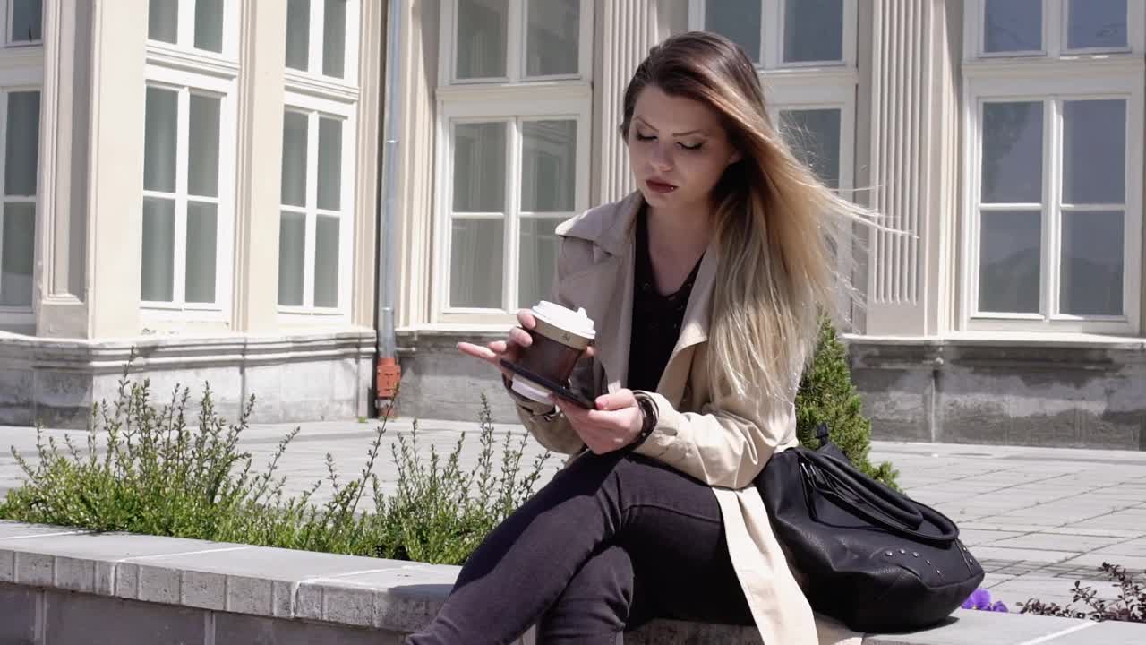 女人在户外放松，喝咖啡和使用平板电脑视频下载