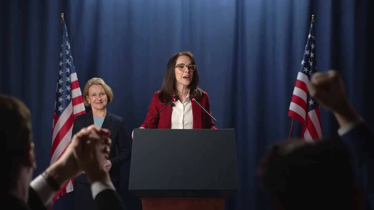 女政治家在鼓舞人心的演讲中，背景是美国国旗视频素材