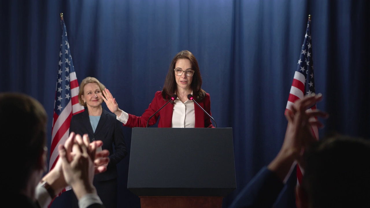 黑发女政治家在红色夹克发表鼓舞人心的演讲，站在基座后面视频素材