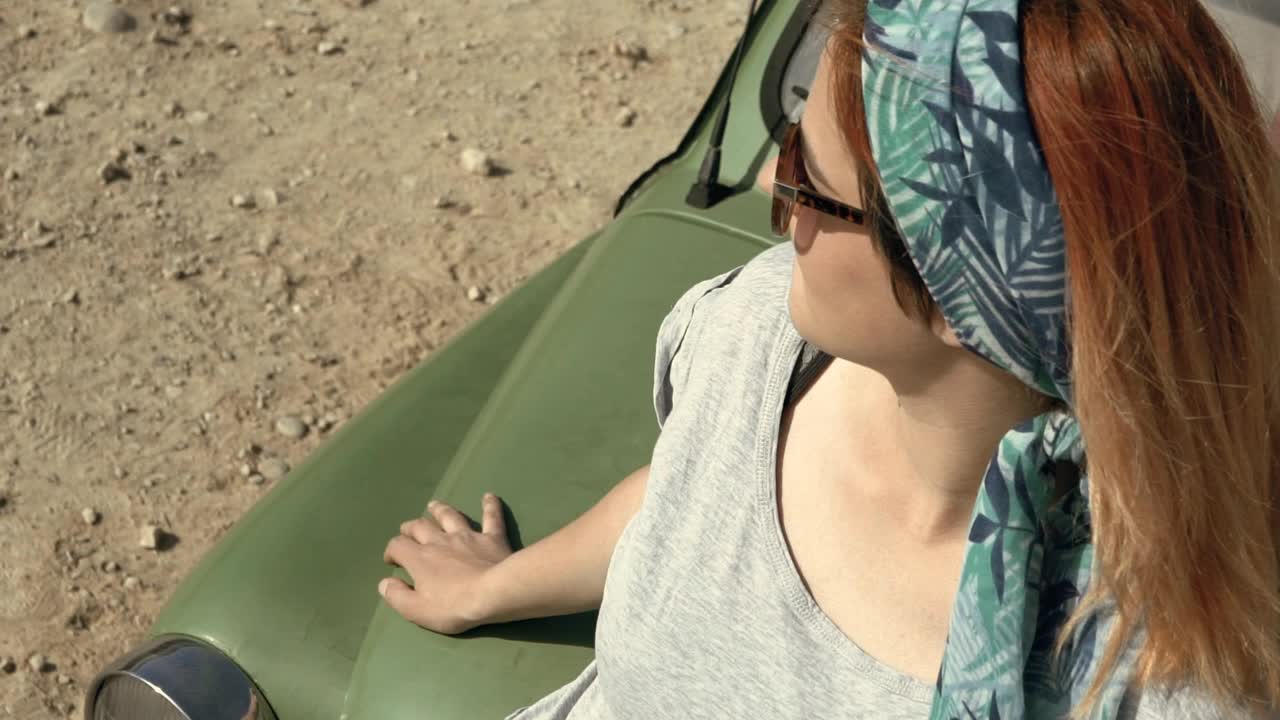 一个红发女人坐在汽车引擎盖上视频下载