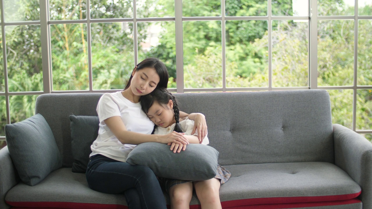 快乐的妈妈在家里的沙发上照顾和拥抱她的女儿视频素材