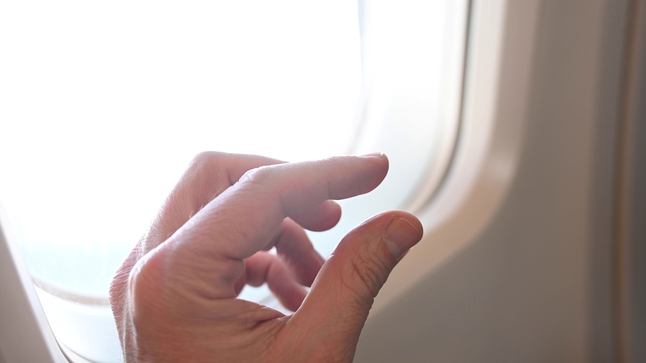 在飞行中，一个无法辨认的人用手指在飞机窗口边做了一个测量小东西的手势。视频下载