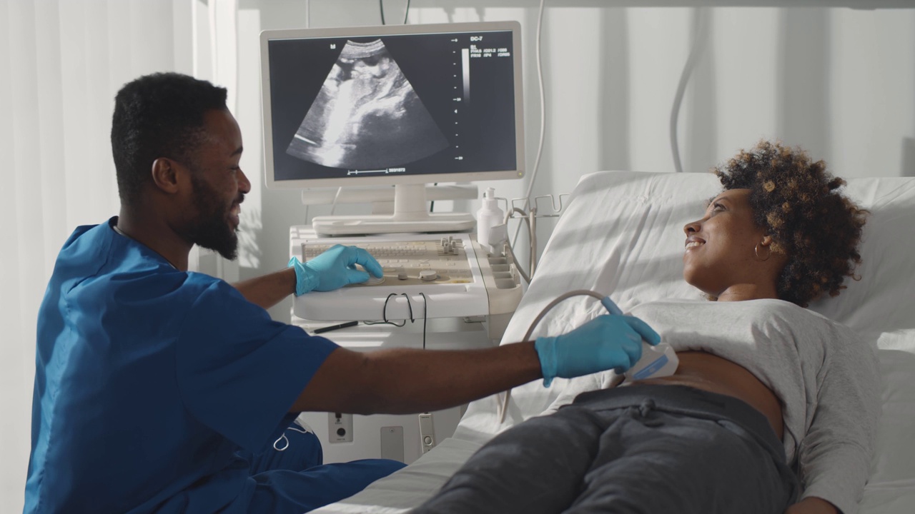 年轻的非洲男性医生，看着屏幕上正在给孕妇做超声波扫描视频素材