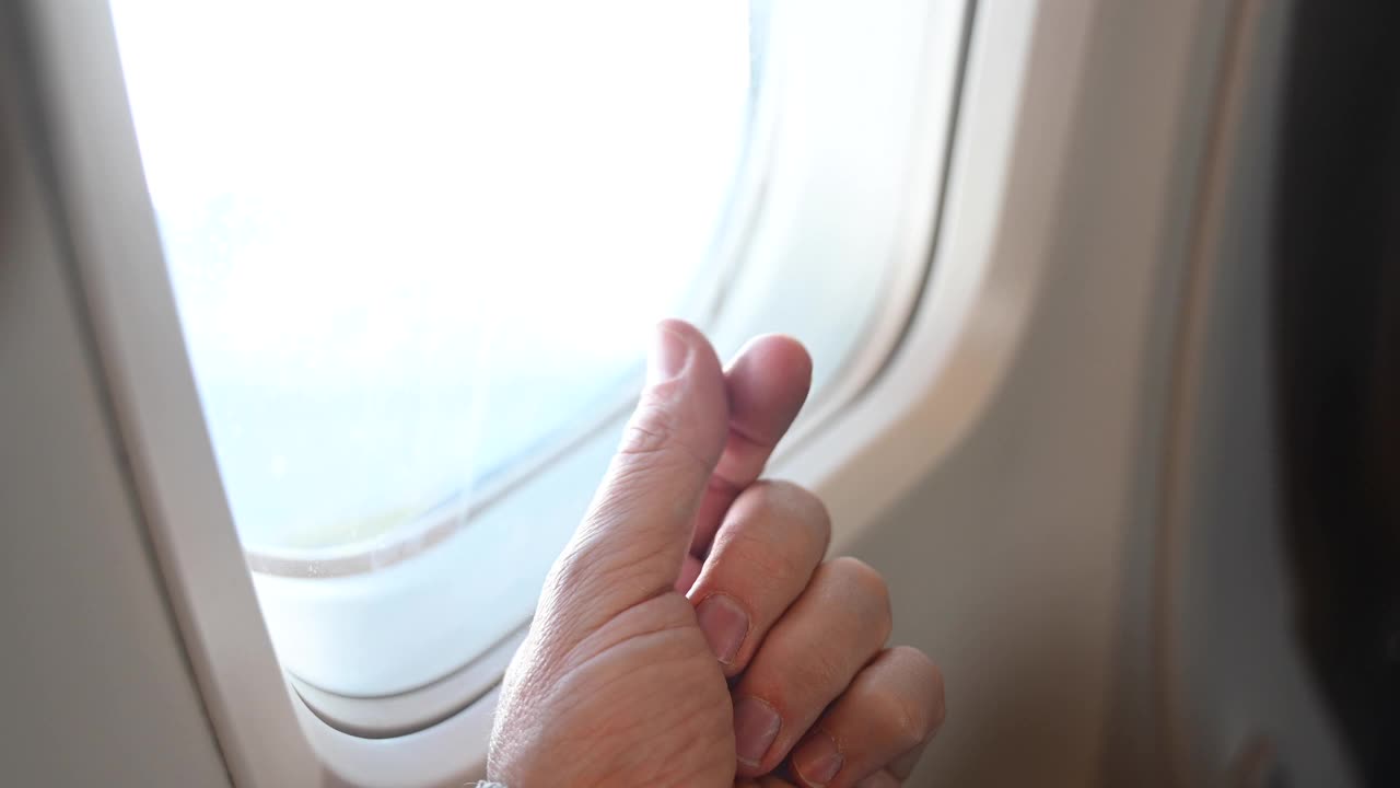 坐飞机变得很贵。在飞行中，一个不知名的人在飞机窗口边做储蓄的手势。燃料在全球范围内变得更加昂贵。视频下载