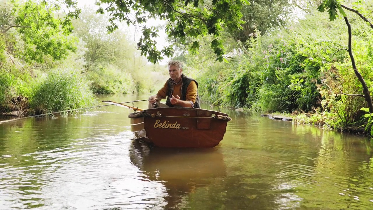 成熟的男人在绿色的夏河上的木船上飞钓视频下载