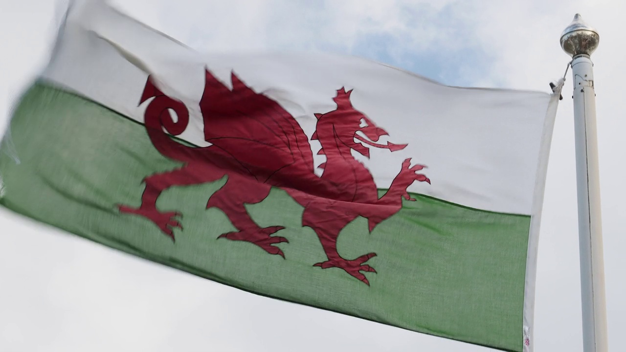 英国威尔士安格尔西岛，一面威尔士国旗和英国国旗在狂风中飘扬。视频下载