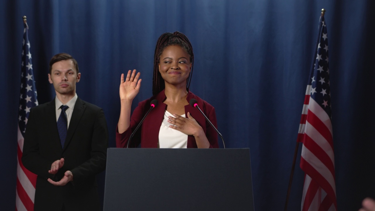 一位身穿红色夹克的年轻黑人女性演讲者在蓝色背景的演讲结束后向观众致谢视频下载