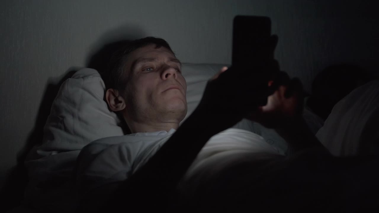 深夜躺在床上使用智能手机的男人视频素材