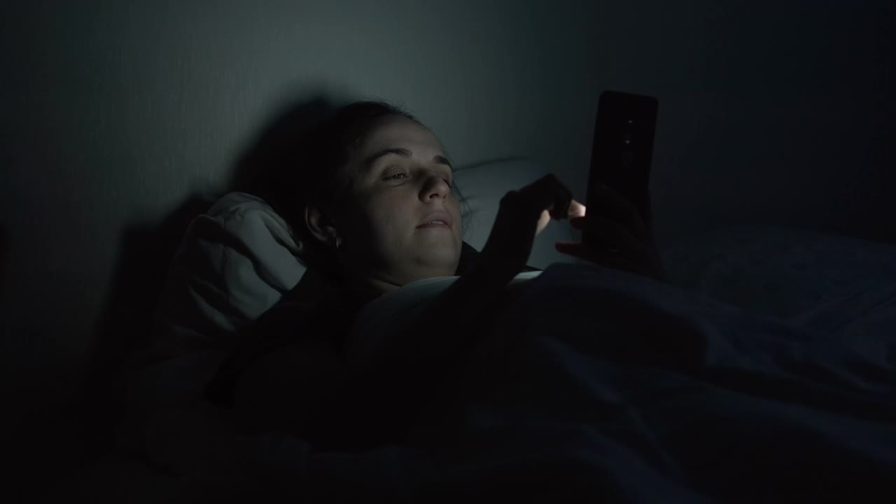 晚上躺在床上用智能手机的女人视频素材