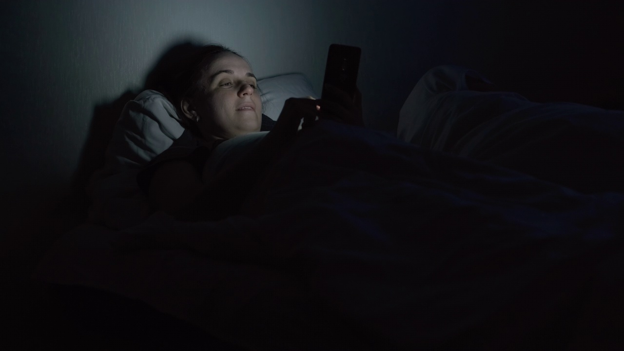 深夜躺在床上使用智能手机的女人视频素材